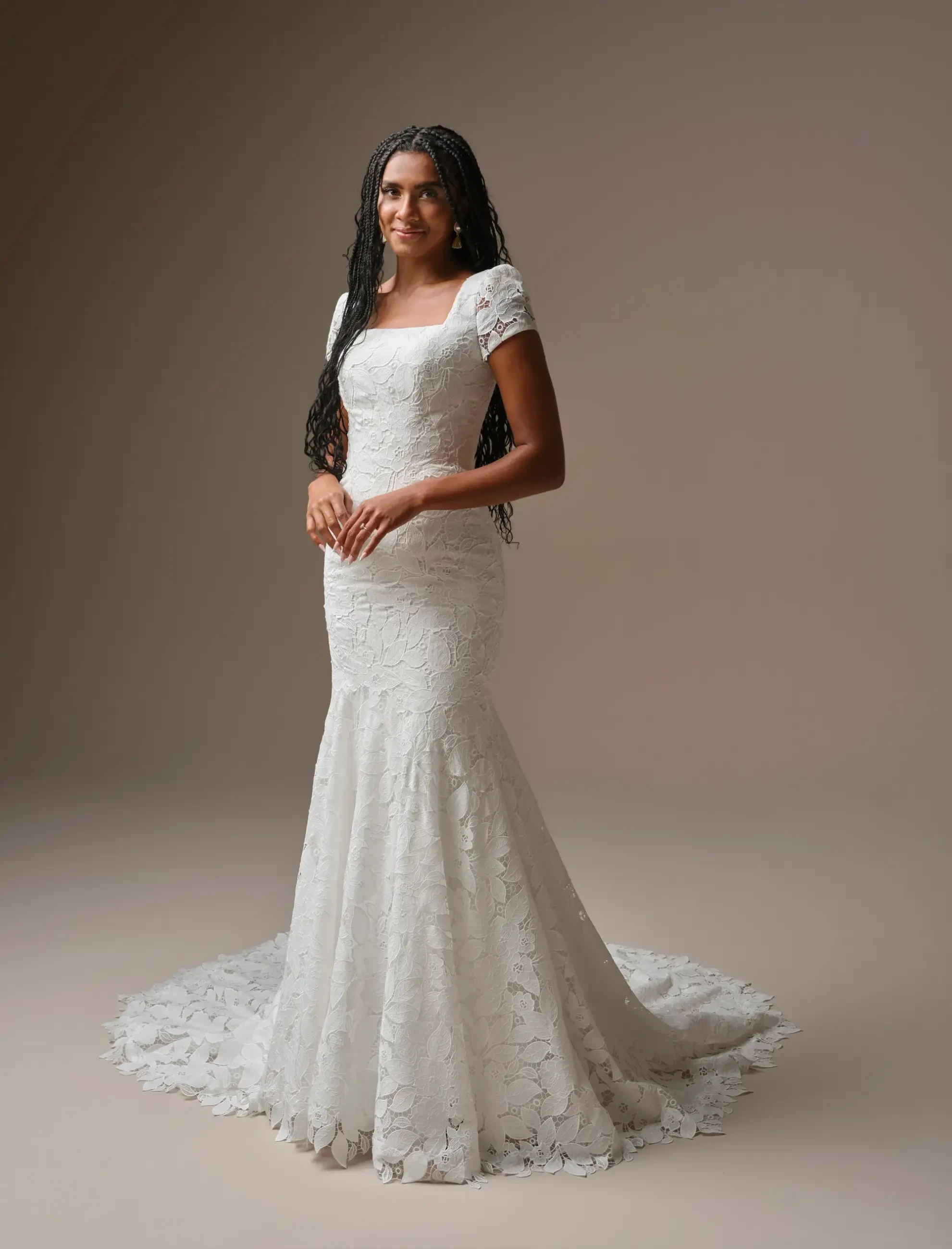 A woman wearing a white lace wedding dress with short sleeves, standing gracefully against a neutral background.