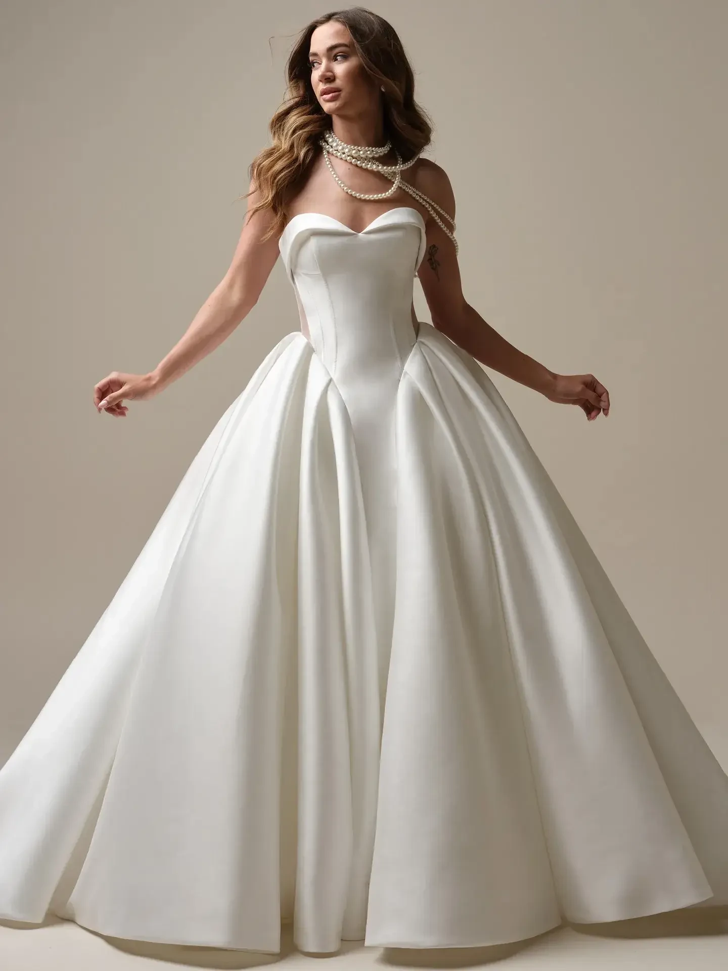 A woman wears an elegant, strapless white ball gown with a structured bodice and full skirt. She is adorned with layered pearl necklaces, exuding a timeless, sophisticated aura.