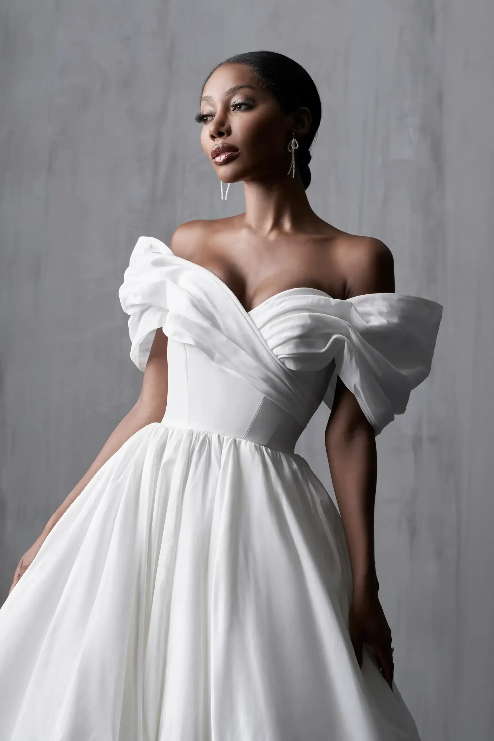 A woman wearing a strapless white gown with puffed sleeves, posed elegantly against a neutral background.