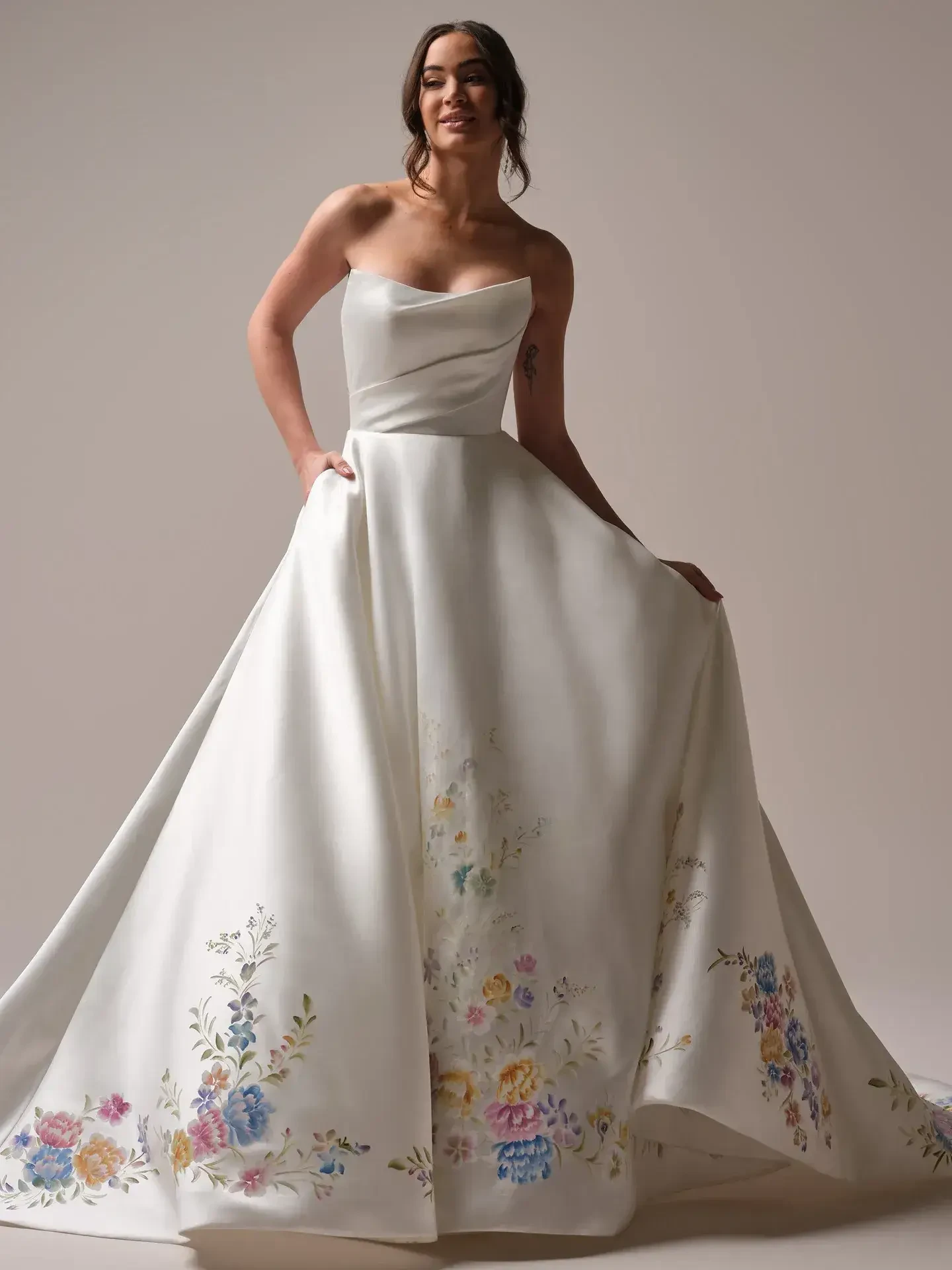 A woman in a strapless white gown with floral embroidery, posing elegantly.